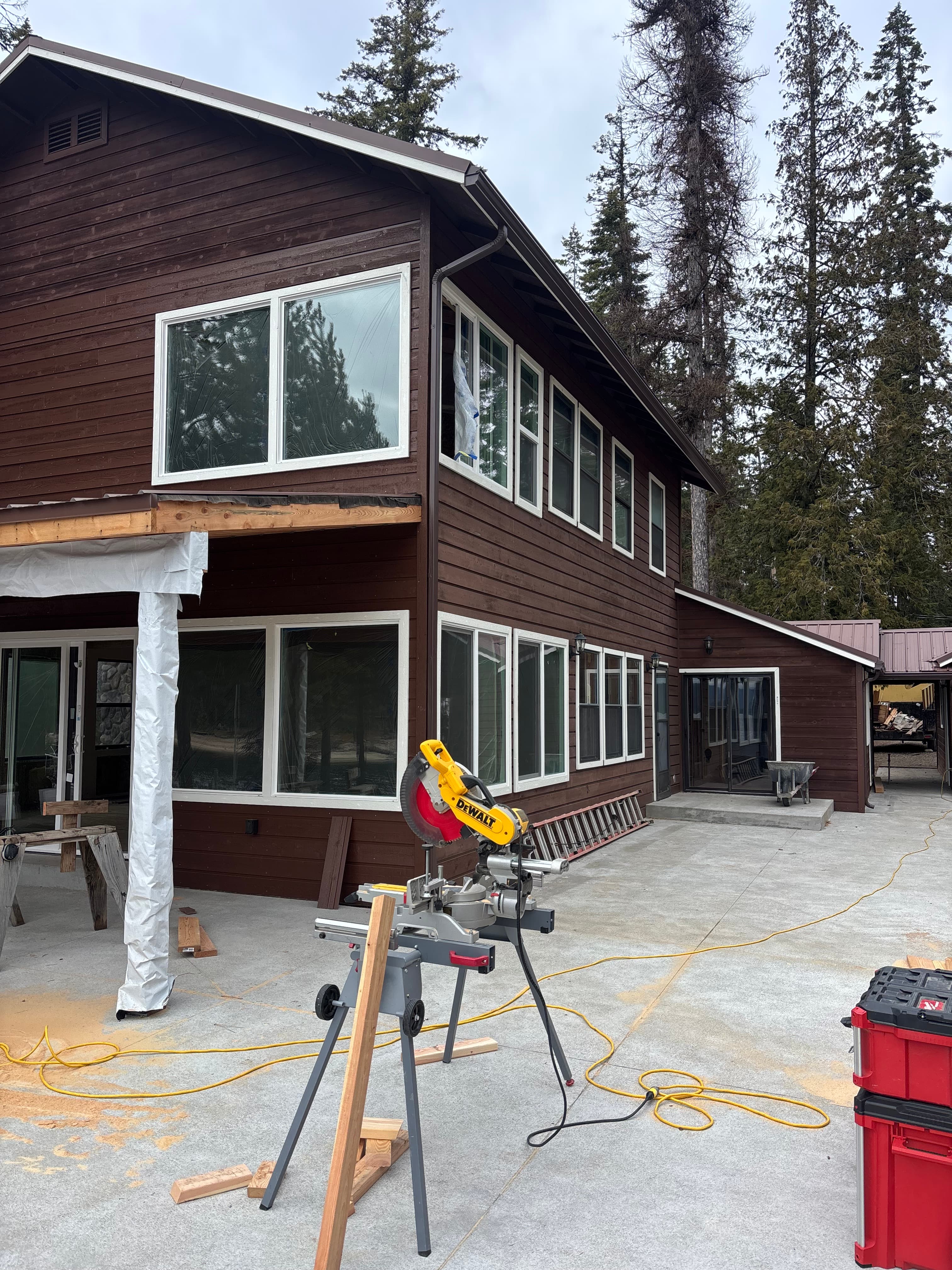 Yellow miter saw on a stand outside a brown wooden house undergoing exterior renovations.