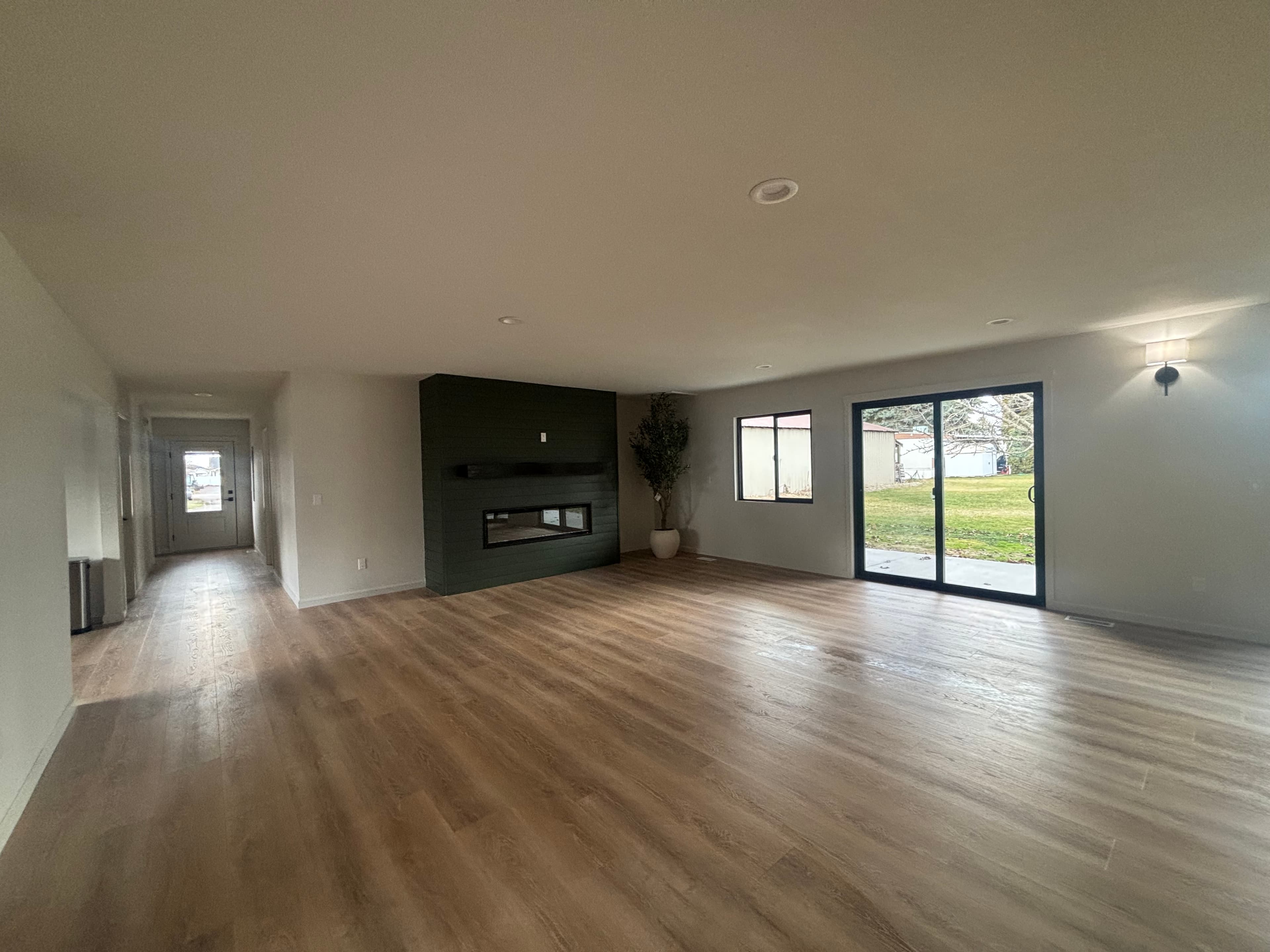 Modern open-concept living space with light wood floors, dark fireplace wall, and sliding glass doors.