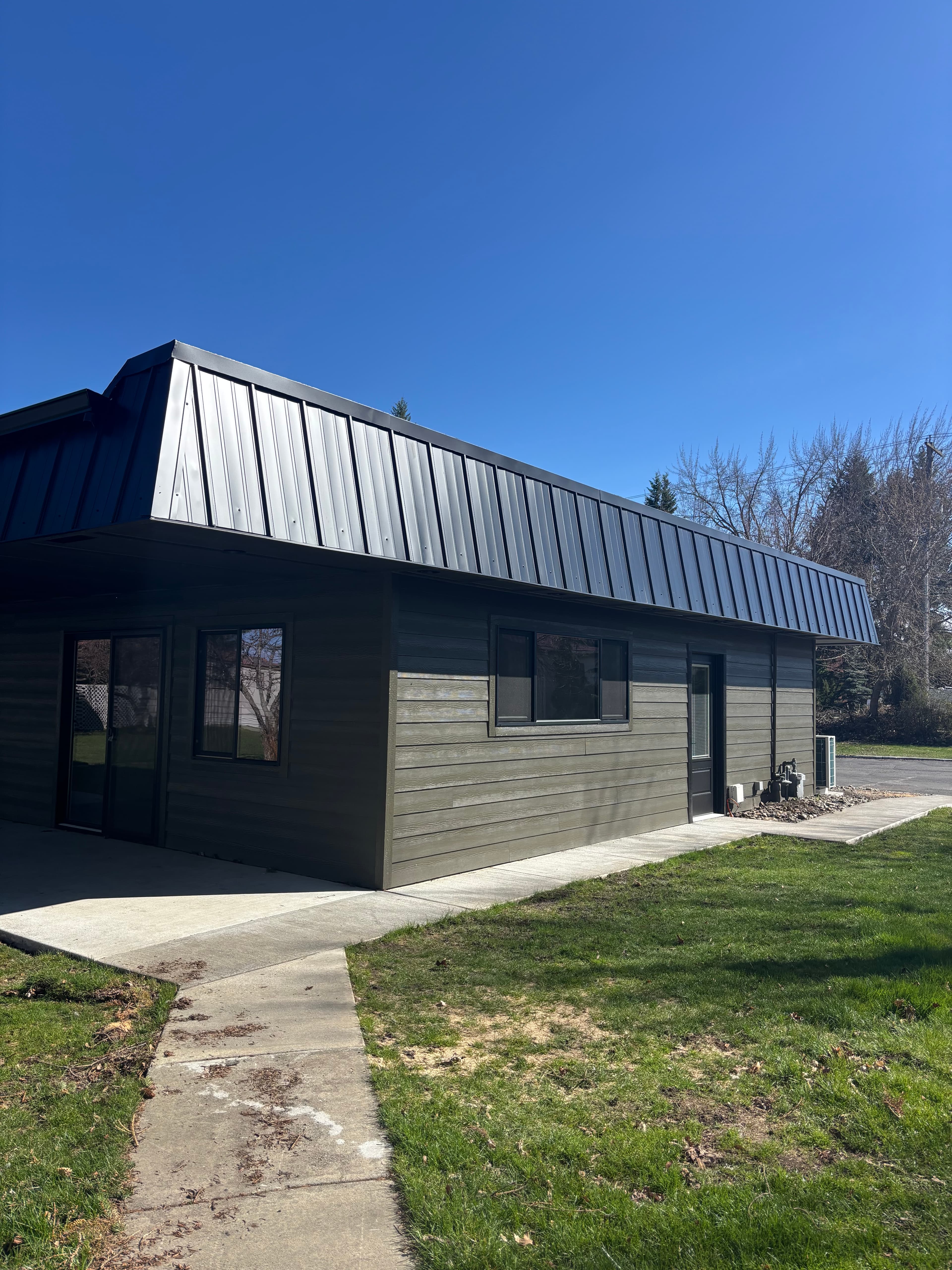 Modern dark grey building with a black metal roof under a clear blue sky.