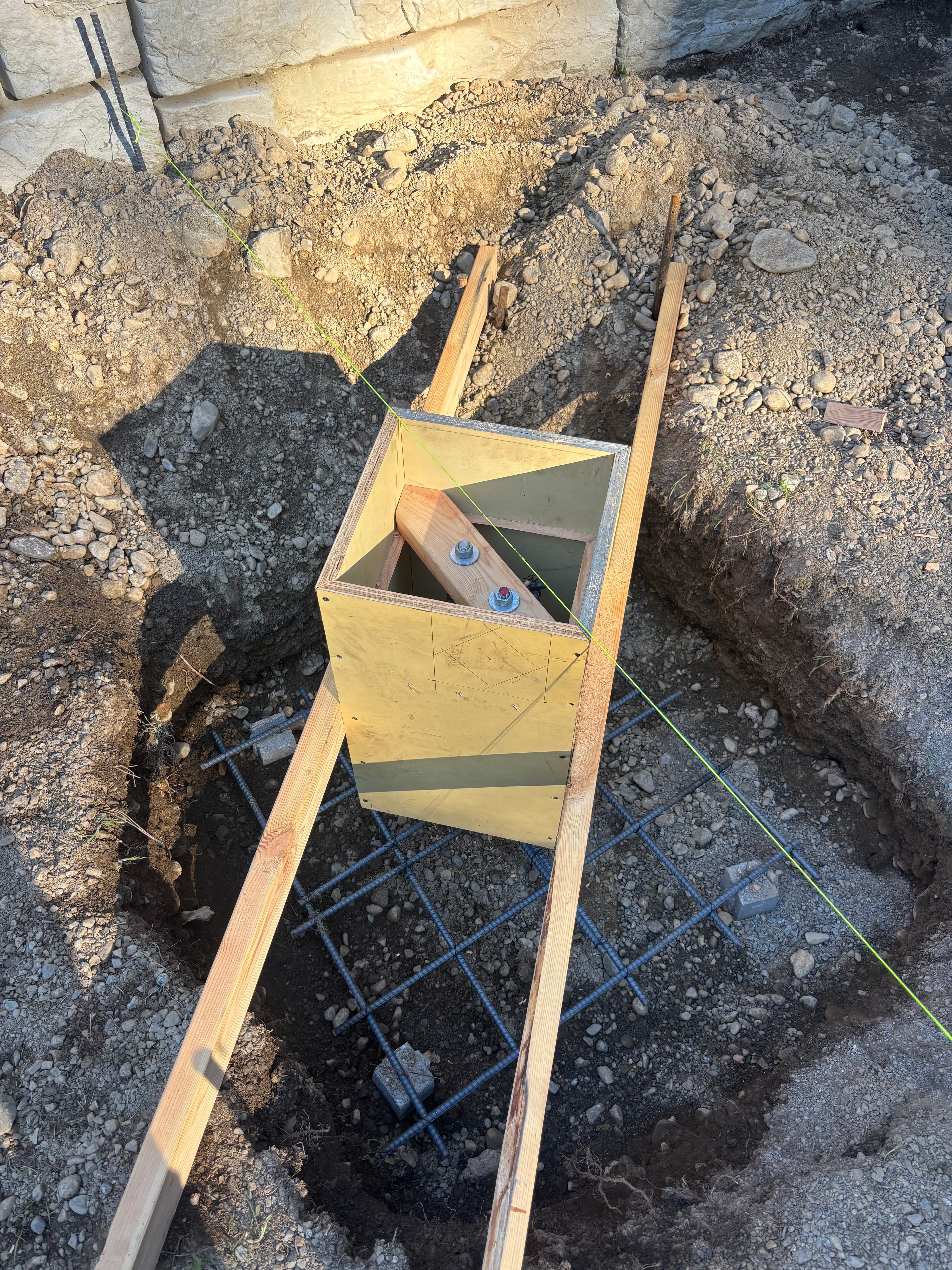 Wooden formwork box over a rebar grid in a construction hole with alignment string.