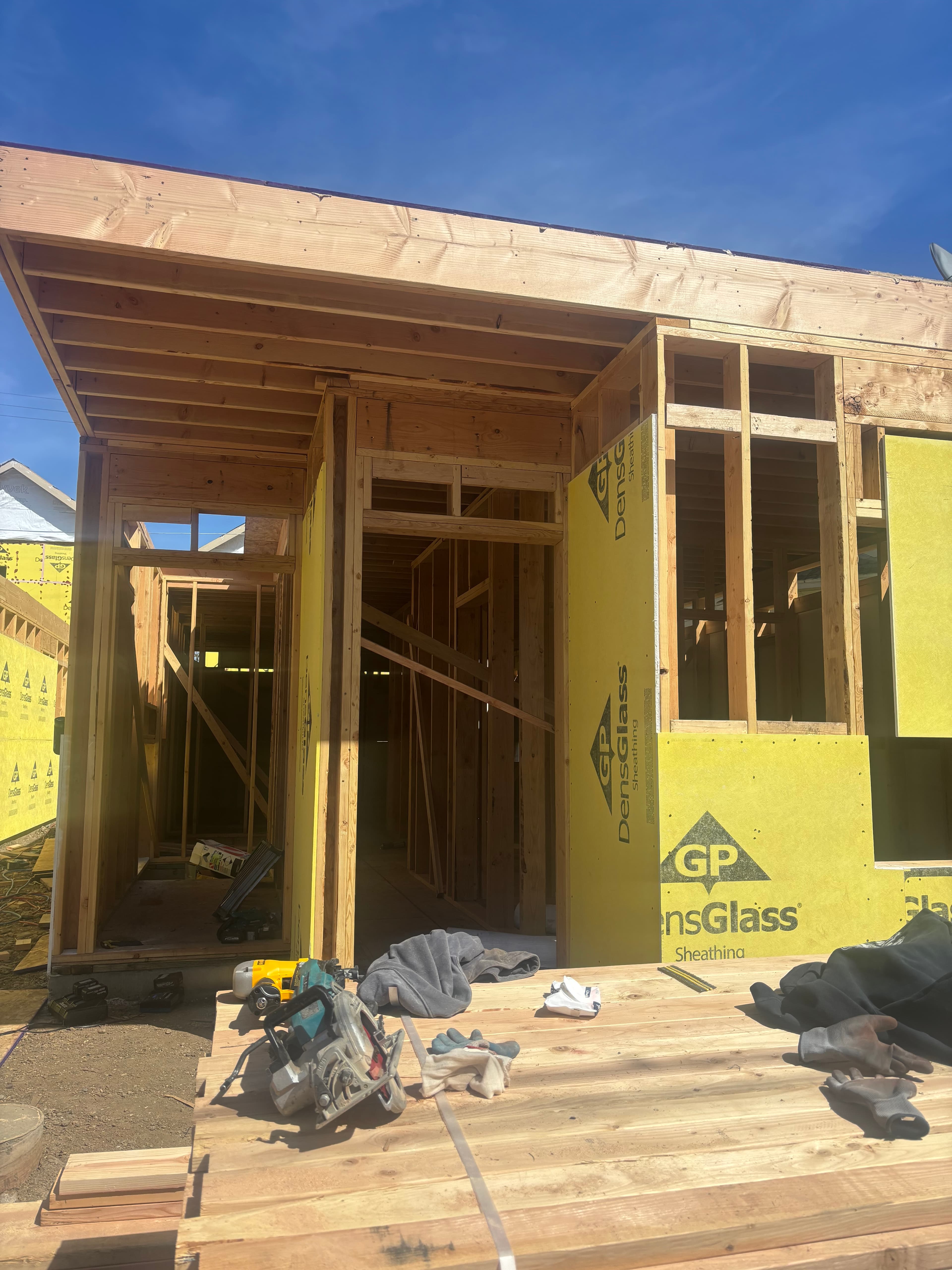 Wooden house framing with yellow sheathing and power tools on a sunny construction site.